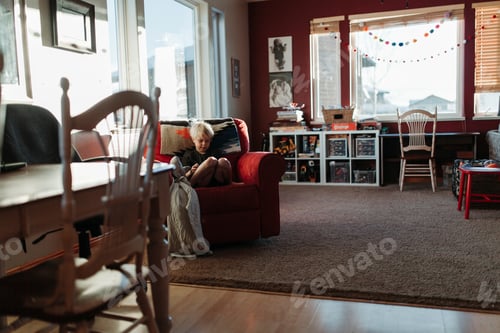 Preview: boy on his phone cozy in a red chair.