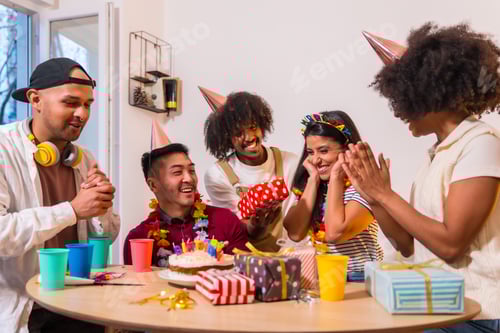 Preview: Multi-ethnic group of friends at a birthday party on the sofa at home with a cake and gifts