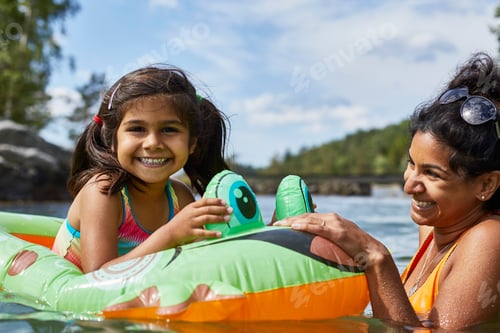 Preview: Mother playing with daughter on inflatable frog in lake