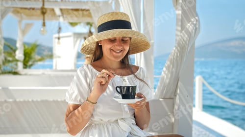 Preview: Young brunette woman relaxing at the sea beach cafe or restaurant and drinking coffee