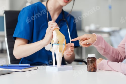 Preview: Caucasian female doctor explain to asian female patient using knee bone model at desk in medical