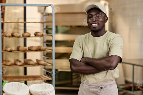Preview: Black young man standing in bakery kitchen with arms crossed and smiling
