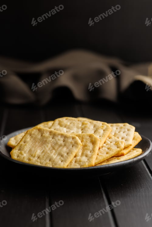 Preview: Salted Crackers on Black Plate Against a Dark Background