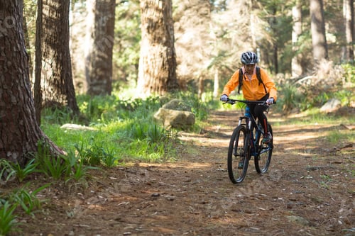 Preview: Woman cyclist riding mountain bike on forest trail wearing jacket, helmet and backpack, copy space