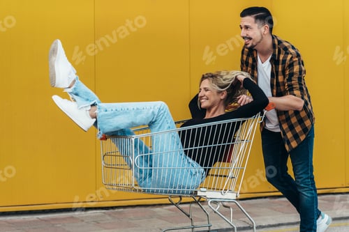 Preview: Young beautiful couple riding in a a supermarket shopping cart