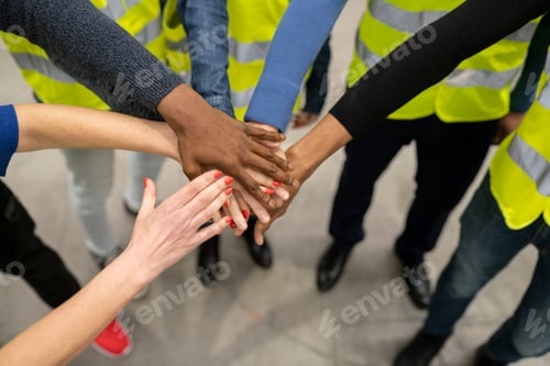 Preview: Close up multiracial group of workers wearing reflective vests with their hands together showing