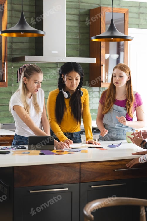 Preview: Teen girls collaborating on school project in modern kitchen, discussing ideas