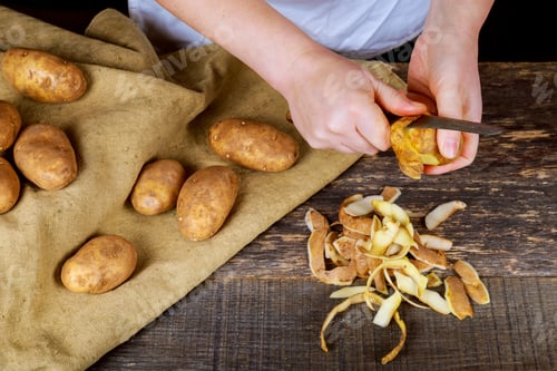 Preview: Woman hands peel potato, peelings on wooden cutting board