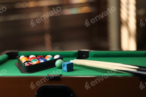 Preview: Many colorful billiard balls in triangle rack, cues and chalk on green table indoors, space for text