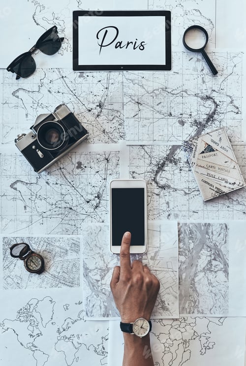 Preview: Planning new destination. Close up top view of man using smart phone in front of the map