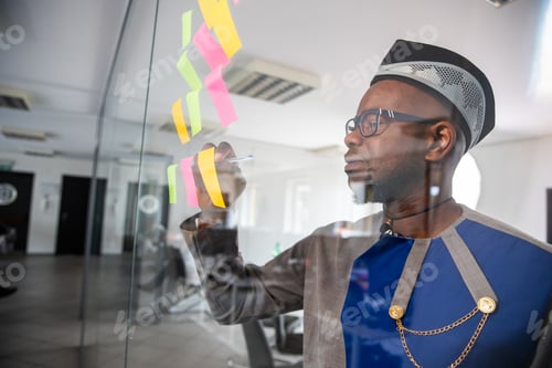 Preview: An African businessman writes on colorful sticky notes hanging on the wall in the office