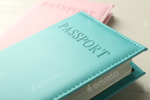 Preview: Two passports in bright covers on white wooden table, closeup