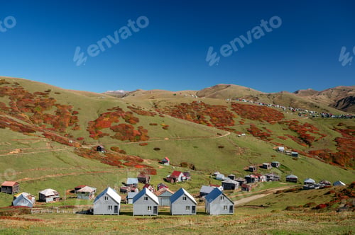 Preview: Beautiful autumn mountain landscape with colorful trees, snow peaks and houses.