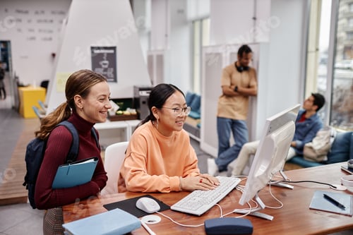 Preview: Students in college library focus on two smiling young girls using computer