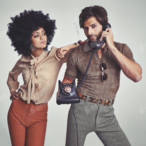 Preview: A beautiful young hippie looking over at a handsome man using a retro telephone