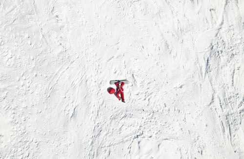 Preview: Top view funny santa claus lying on snowboard and wishing merry christmas. Aerial view.