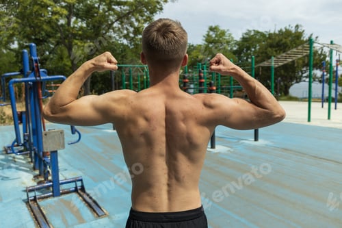 Preview: A man on the background of a sports ground, showing the muscles of his back and arms