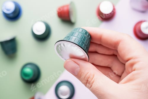 Preview: Female hand hold capsules for coffee machine on green and pink background, top view.
