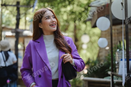 Preview: Young businesswoman smiling and walking in a park during a sunny day