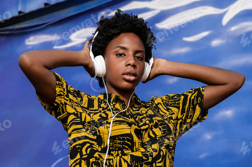 Preview: Young african american woman with short hair and modern clothes listening to music with headphones