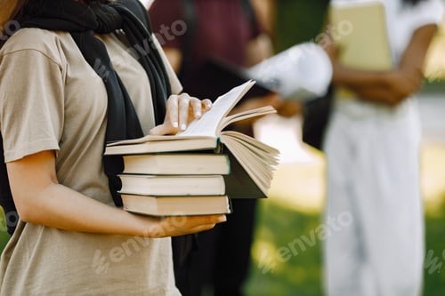Preview: Three international students standing in a park and holding a books