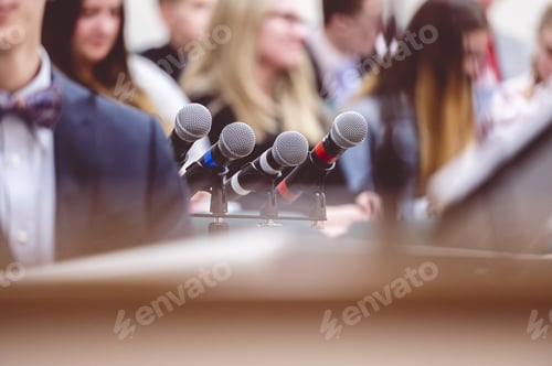 Preview: Selective focus shot of microphones next to a rostrum on a stage