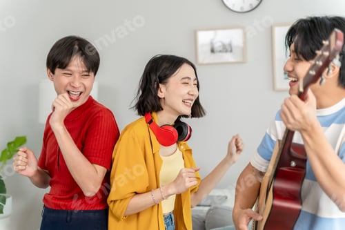 Preview: Diverse Asian friends playing guitar and dancing in living room at home.