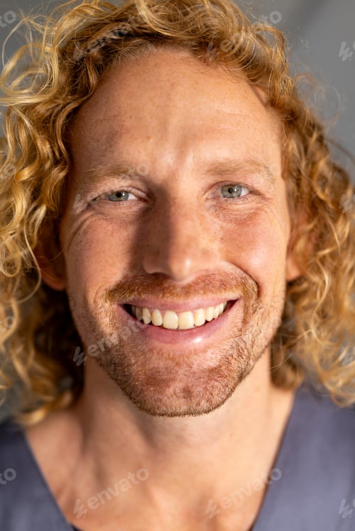 Preview: Portrait of happy caucasian male doctor with curly hair in corridor at hospital