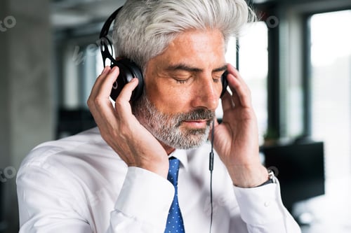 Preview: Mature businessman with headphones in the office.