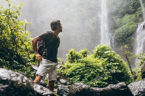Preview: Male hiker near waterfall during rain