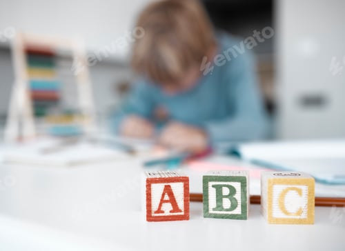 Preview: Closeup of wooden toy blocks on a table at home. A little boy blurred in the background, playing, d
