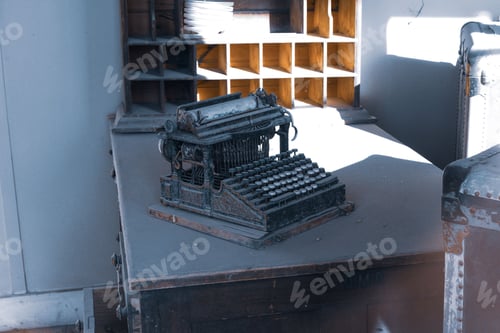 Preview: Old, dusty 1870 typewriter on a desk in a vintage office setting with shelves in the background