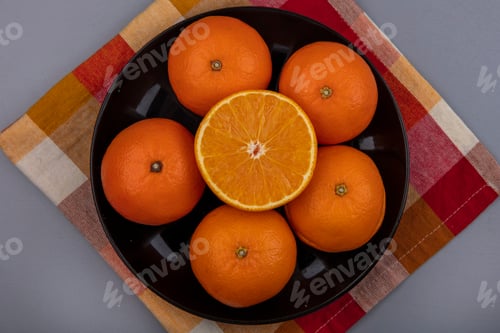 Preview: top view oranges on a black plate on a checkered towel on a gray background