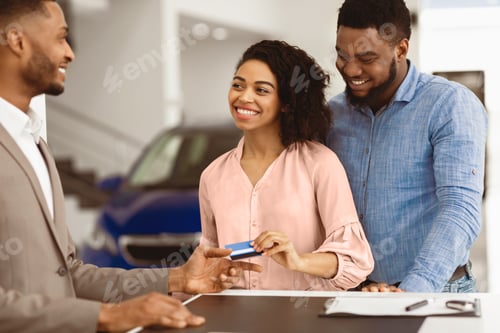 Preview: Spouses Giving Credit Card To Salesman Standing In Automobile Dealership