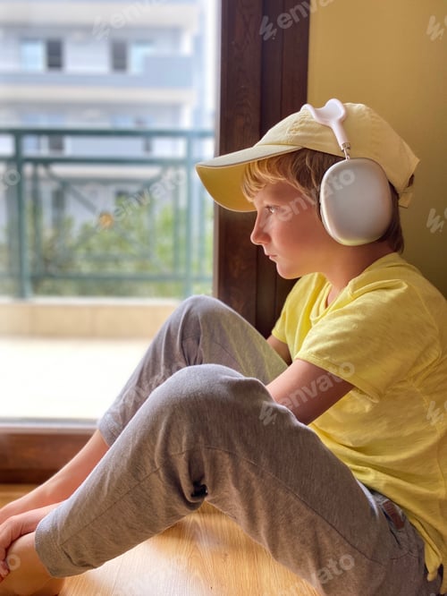 Preview: Thoughtful Child with Headphones Seated by a Window