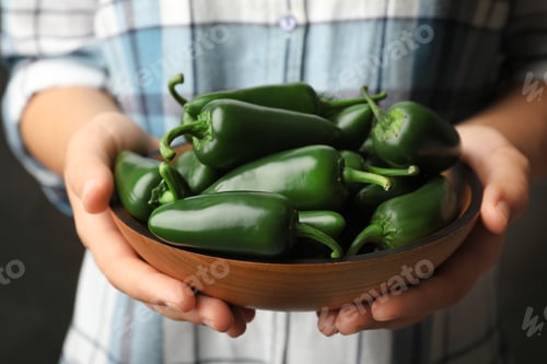 Preview: Young woman holding wooden bowl with green hot chili peppers, closeup