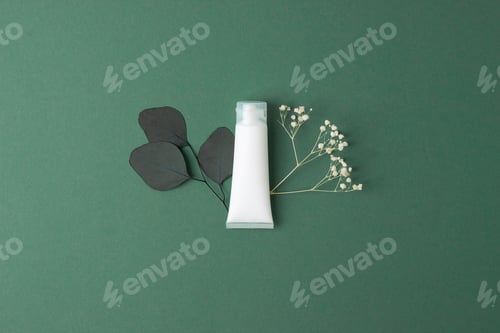 Preview: White tube of cosmetic cream with flowers and green leaves on green olive background