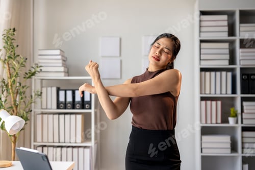 Preview: A woman is stretching in a cubicle with a lot of books around her