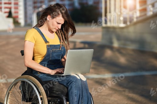 Preview: stylish disabled girl in casual clothes concentrated on working with laptop