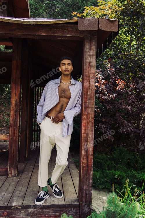 Preview: full length of african american man in stylish clothes looking at camera in wooden gazebo
