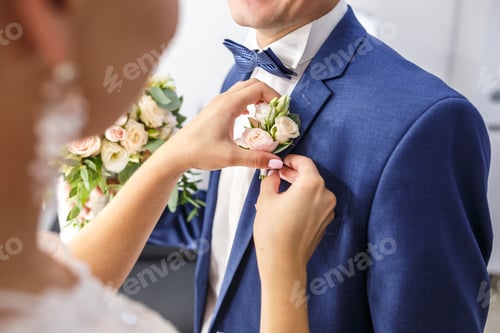 Preview: bride puts groom on boutonniere from pink and whote rose on wedding day