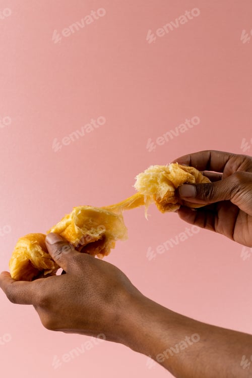Preview: Vertical image of hands of african american man tearing croissants on pink background