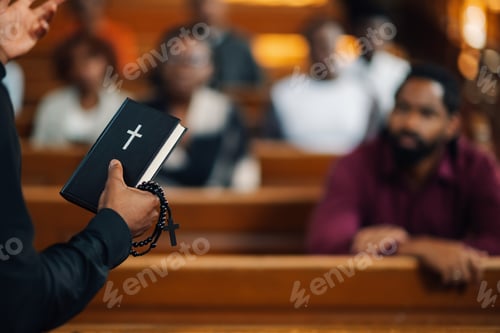 Preview: Priest holding holy bible and rosary preaching to congregation