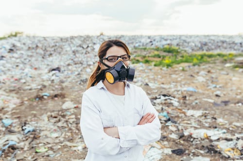 Preview: Female scientist in a protective respirator mask at a landfill assesses the level of environmental