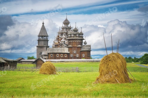 Preview: Field with haystacks. In the background a wooden famous Kizhi Pogost at summer cloudy day.