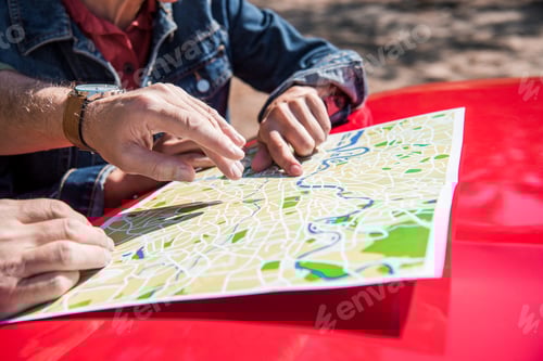 Preview: cropped view of senior couple of travelers standing near car with map in sunny day