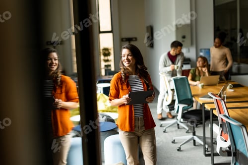Preview: Young woman standing with digital tablet in front of her team at the office