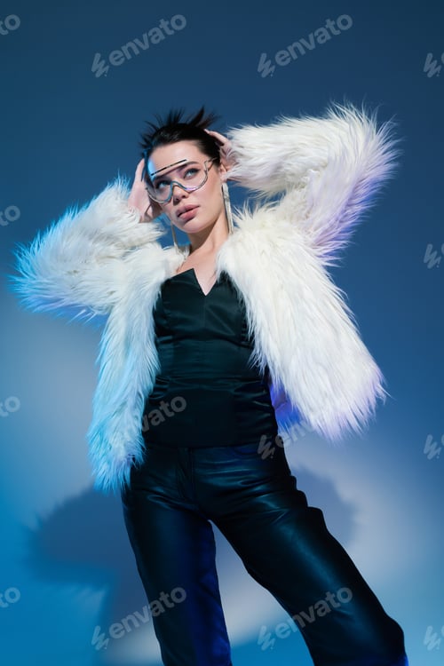 Preview: model in black corset and trendy faux fur jacket posing with hands behind head on blue background