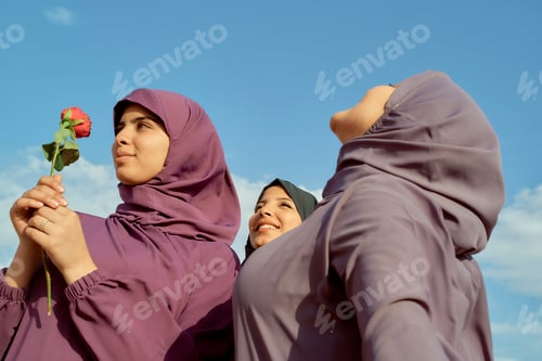 Preview: Three women in purple hijabs enjoy a sunny day outdoors with one holding a red rose, Morocco