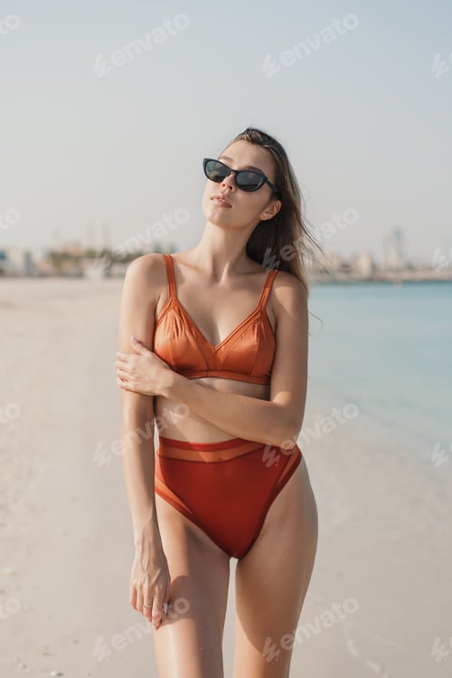 Vista previa: Mujer joven vestida en bikini naranja de pie en la playa